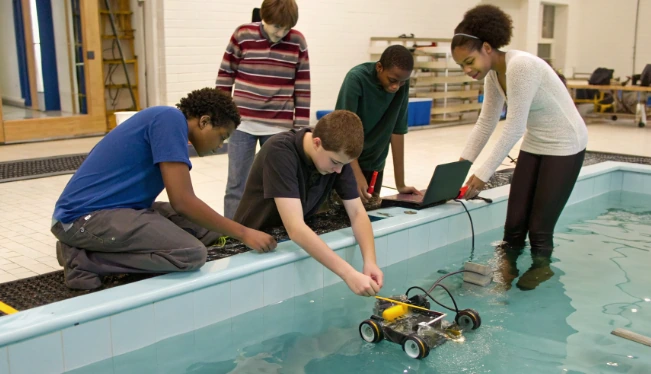 School club students program and test an underwater robot at a pool, showing team-based WaterBotics-style robotics education in action
