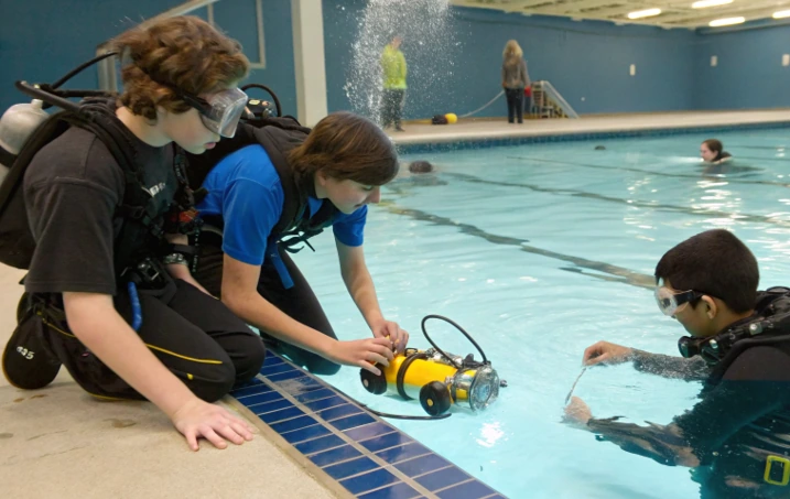 Students in scuba gear launching an underwater robot at a pool, showing what distinguishes the WaterBotics program from other robotics programs
