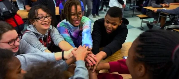 Middle school and high school students putting their hands together in a classroom, showing teamwork on a hands-on STEM water robotics project
