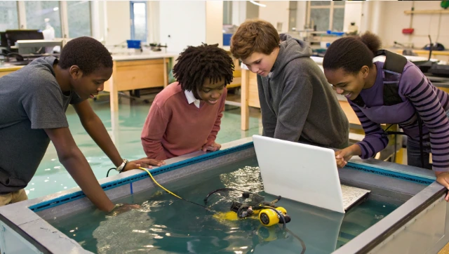 Group of students with a laptop testing an underwater robot in a classroom water tank, illustrating the WaterBotics curriculum and STEM learning in action
