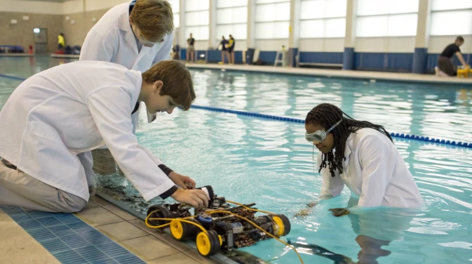 Students in lab coats testing a team-built underwater robot in a pool, showing real WaterBotics-style STEM project in action
